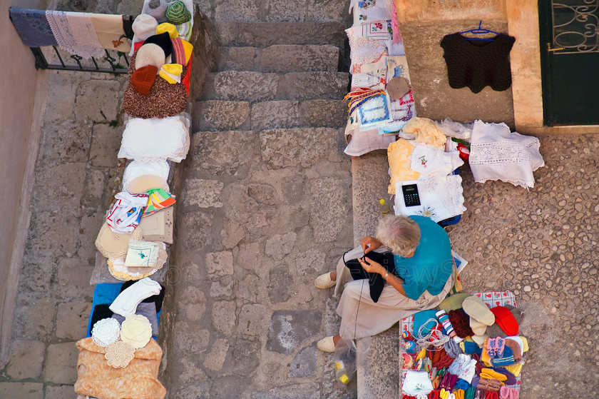 Old woman and cushion covers 
 Old woman embroidering cushion covers on street in Dubrovnik, Croatia, viewed from above 
 Keywords: Street, old woman, seamstress, Dubrovnik, Croatia, multi coloured, cushions, cushion covers